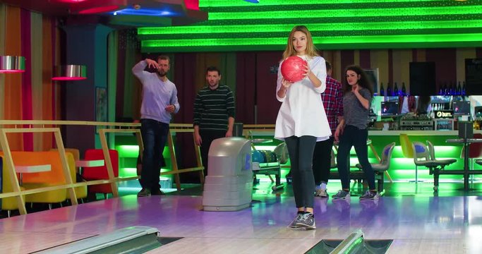 Young woman playing bowling game and throwing ball to lane 4k leisure video. Friends playing, girl happy for win. Lucky shot hit. Hobby and competitions