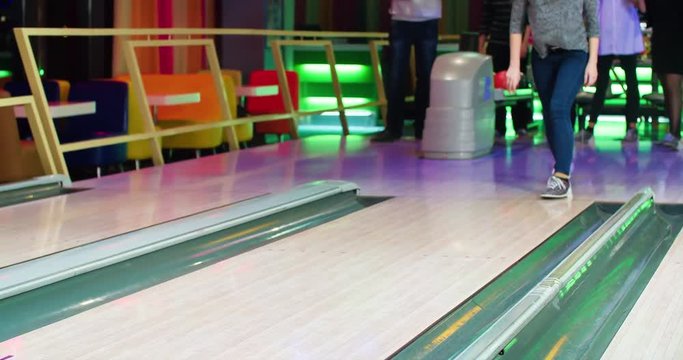 Young woman playing bowling game and throwing ball to lane 4k leisure video. Friends playing, girl happy for win. Lucky shot hit. Hobby and competitions