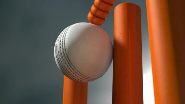 An ultra motion close up of a white leather stitched cricket ball hitting orange wickets with dirt particles emanating from the impact at night