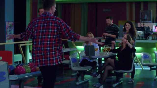 Friends playing and having fun at bowling HD slow-motion leisure video. Group of young man and woman at bar table celebrates winning.