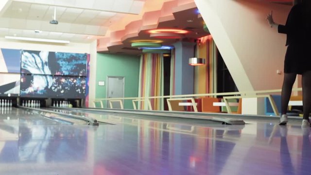 Woman playing bowling game and throwing ball to lane HD leisure video. Girl rolling ball on alley back floor view. Hobby and competitions