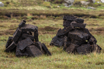 North Coast, Scotland - June 6, 2012: Closeup of two short stacks of blocks of black peat, the local fuel. Heaps on green-brown grassy field.