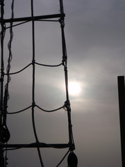 An abstract view of old rigging on a sailing vessel used in tourism tours with the cloud covered sun in the background.