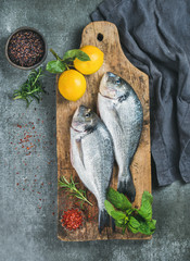 Fresh uncooked sea bream or dorado fish with lemon, herbs and spices in bowls on rustic wooden...
