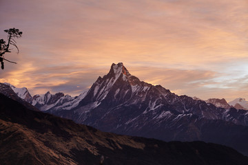 Fototapeta na wymiar Beautiful landscape of Mount Machapuchare covered with snow and ice and illuminated with pink sunlight. Craggy snowy peak rising above desolate valley. Frosty winter morning high in mountains