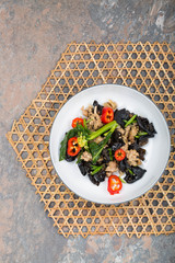 Wood ear mushroom stir-fry with ground meat and red peppers. Brown stone background. Bamboo placemat. 