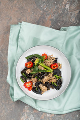 Wood ear mushroom stir-fry with ground meat and red peppers. Brown stone background. A green napkin under the plate. 