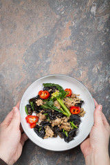 Wood ear mushroom stir-fry with ground meat and red peppers. Brown stone background. Female hands holding a plate. 