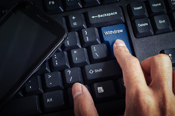 business concept shows the smartphone as well as the fingers that press WITHDRAW on the keyboard