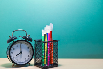 Group of colorful pen and alarm clock on wood table.
