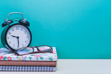 Alarm clock,glasses and Books on wooden table with copy space.Green background.