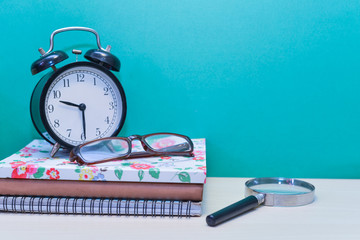 Alarm clock,glasses,magnifier glass and Books on wooden table with copy space.Green background.