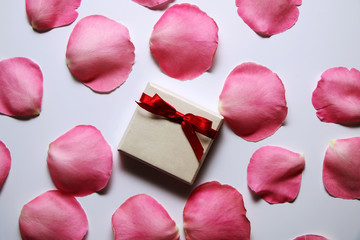 White gift box with a red bow and pink rose petals on white background.