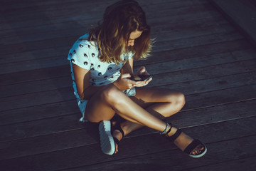 young cute woman using phone,sitting at a cafe holding a smartphone,answering texts,phone calls,letters,posts photos in instagram,outdoor portrait, close up, elaborated and bracelets on the hands