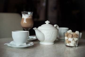 Teapot, two cups, sugar bowl and glass of shake on the table