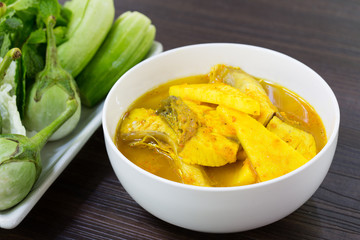 Yellow curry snapper fish with coconut shoots, thai food and fresh vegetable in white dish on brown wooden plate / selective focus..