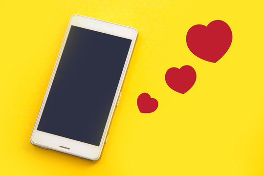 White Smart Phone And Red Hearts On Yellow Background.Concept Of Love Connection