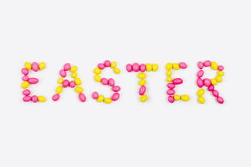Lettering «Easter» is made with pink and yellow candies  on white background