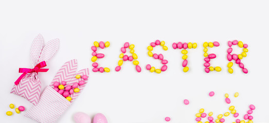 Lettering «Easter» is made with pink and yellow candies   and bunny treat bags on white background