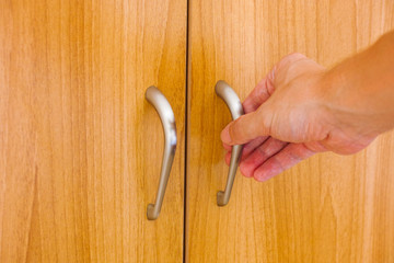 Person hand ready to open wardrobe door with clothes