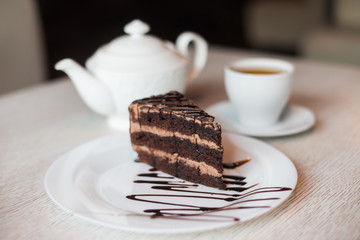 Plate with slice of chocolate cake, teapot and cup with green tea are on the table
