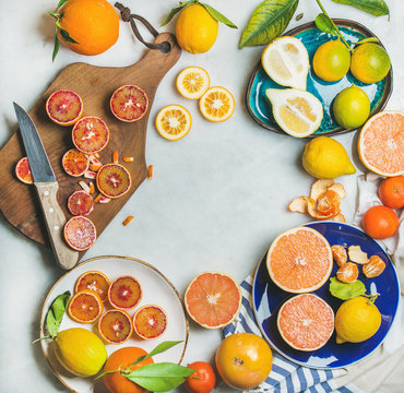 Natural fresh citrus fruits on wooden rustic board, colorful ceramic plates over grey marble table background, top view, copy space