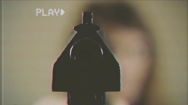 VHS retro fake shot: a woman pointing a gun in front of a victim. Muddy point-of-view shot, close-up on the barrel.
