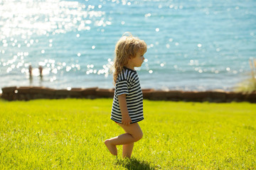 Fototapeta premium Cute baby boy in striped tshirt walks on green grass