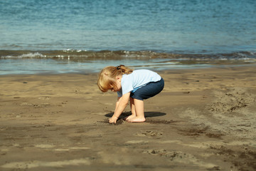 Cute baby boy plays with sand on sandy beach