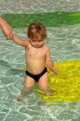 Cute baby boy swims in outdoor pool with mothers help