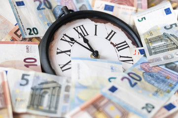 Fuenf Minuten vor zwoelf Uhr / Euro Geldscheine und eine Uhr, die Zeiger stehen fuenf Minuten vor zwoelf.
