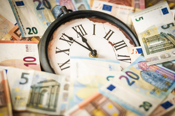 Fuenf Minuten vor zwoelf Uhr / Euro Geldscheine und eine Uhr, die Zeiger stehen fuenf Minuten vor zwoelf.