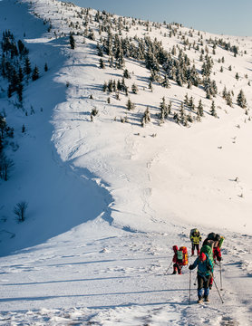 A group of tourists with backpacks climb to the summit of snowy