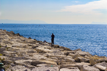 Fototapeta na wymiar alone fisherman with rod on the rocks, Gulf of Naples, Italy
