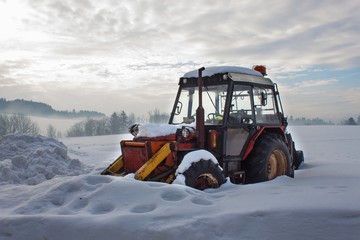 Old tractor under the snow. Snow calamity in transport. Frozen diesel engine.