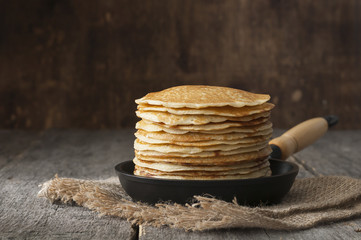Stack of pancakes on a cast-iron frying pan,on wooden background. Style rustic. - obrazy, fototapety, plakaty