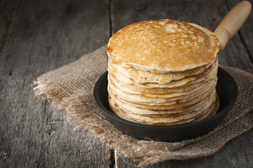 Stack of pancakes on a cast-iron frying pan,on wooden background. Style rustic. - obrazy, fototapety, plakaty