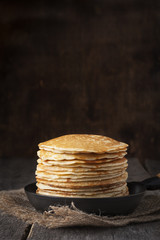 Stack of pancakes on a cast-iron frying pan,on wooden background. Style rustic.