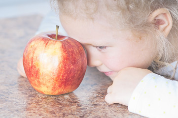 child sad looks on the red ripe apple on the brown surface of marble, poor appetite