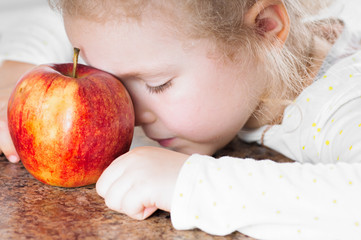 child sad looks on the red ripe apple on the brown surface of marble, poor appetite