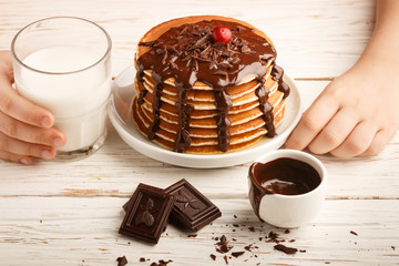 Pancake with chocolate on a white plate. Delicious Breakfast.  The child eats at the table. Selective focus
