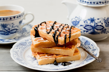 Belgian waffles with chocolate syrup on porcelain plate with blue decor.