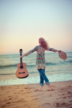 Back view of a beautiful blond female playing guitar on the beach, sunset sunny blue sky outdoors background