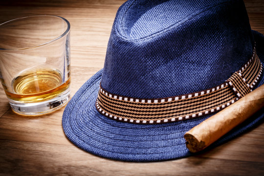 blue hat with cigar and expensive drink of whisky or rum on wooden floor