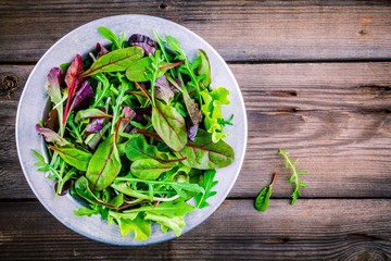 Fresh salad with mixed greens on wooden background