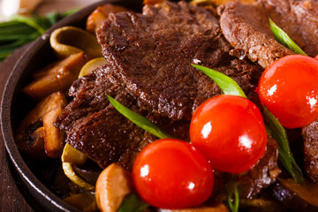 Fried meat in a pan with cherry tomatoes