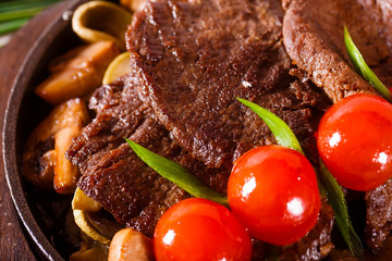 Fried meat in a pan with cherry tomatoes