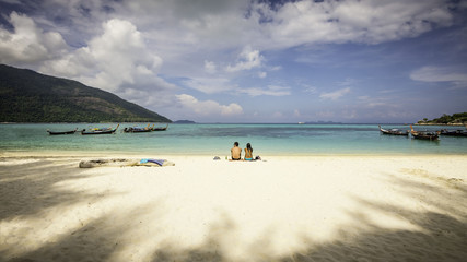Man and woman sitting on the beach, sunbathing and sipping beer. at Koh Lipe,Thailand.