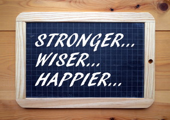The words Stronger, Wiser, Happier in white text on a blackboard as a reminder of our aspirations...