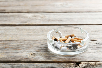 Cigarette butts with ash in ashtray on grey wooden table